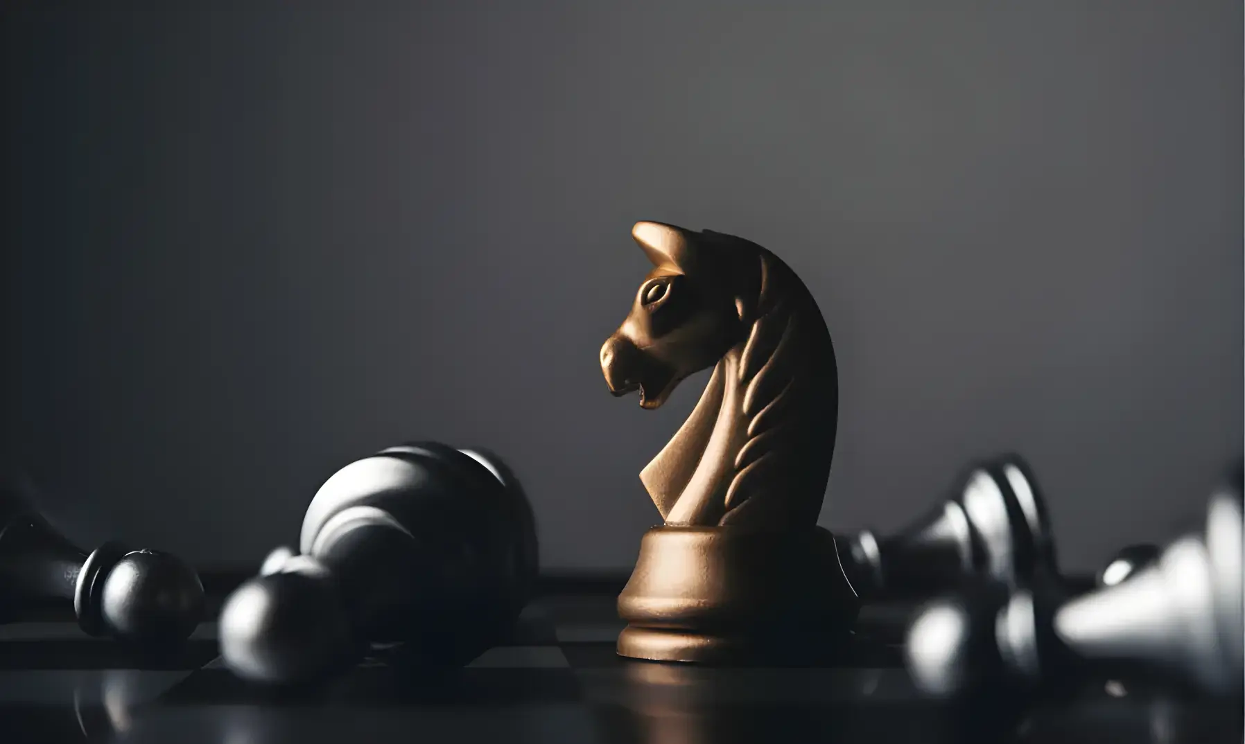 Monochrome image of a black knight chess piece standing upright among fallen pawns on a chessboard. Dramatic contrast and a contemplative tone.