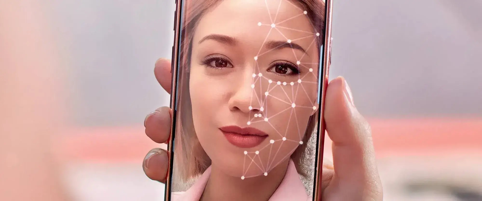 A person holds a smartphone showing a facial recognition interface with digital patterns overlaying their face, conveying a sense of technology and security.